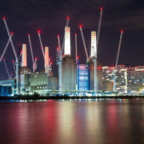 Battersea Power Station lit up at night with construction cranes around it.